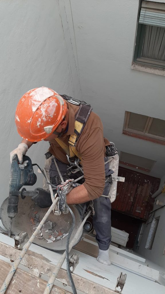 Técnico trabajando en fachada con arnés y cuerdas de seguridad