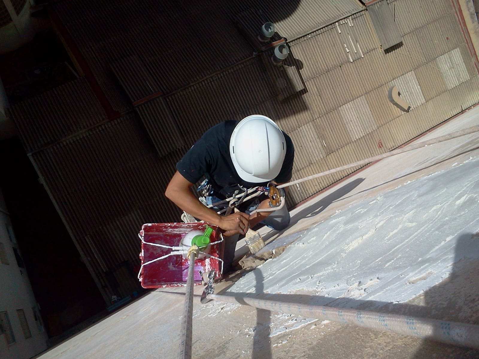 Técnico aplicando impermeabilizante en cubierta plana con arnés