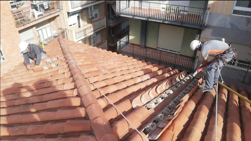 Dos técnicos reparando tejado de tejas con arneses